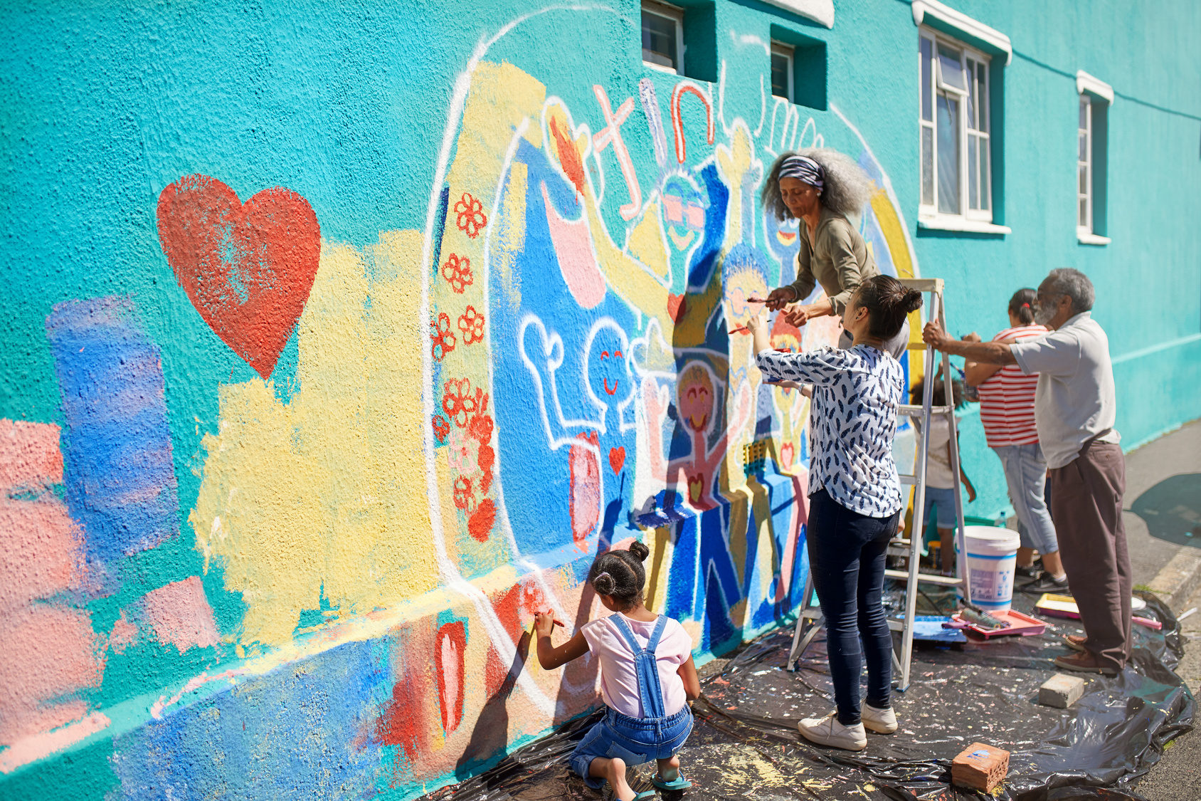 Personnes d'âges différents peignant une grande fresque colorée sur un mur